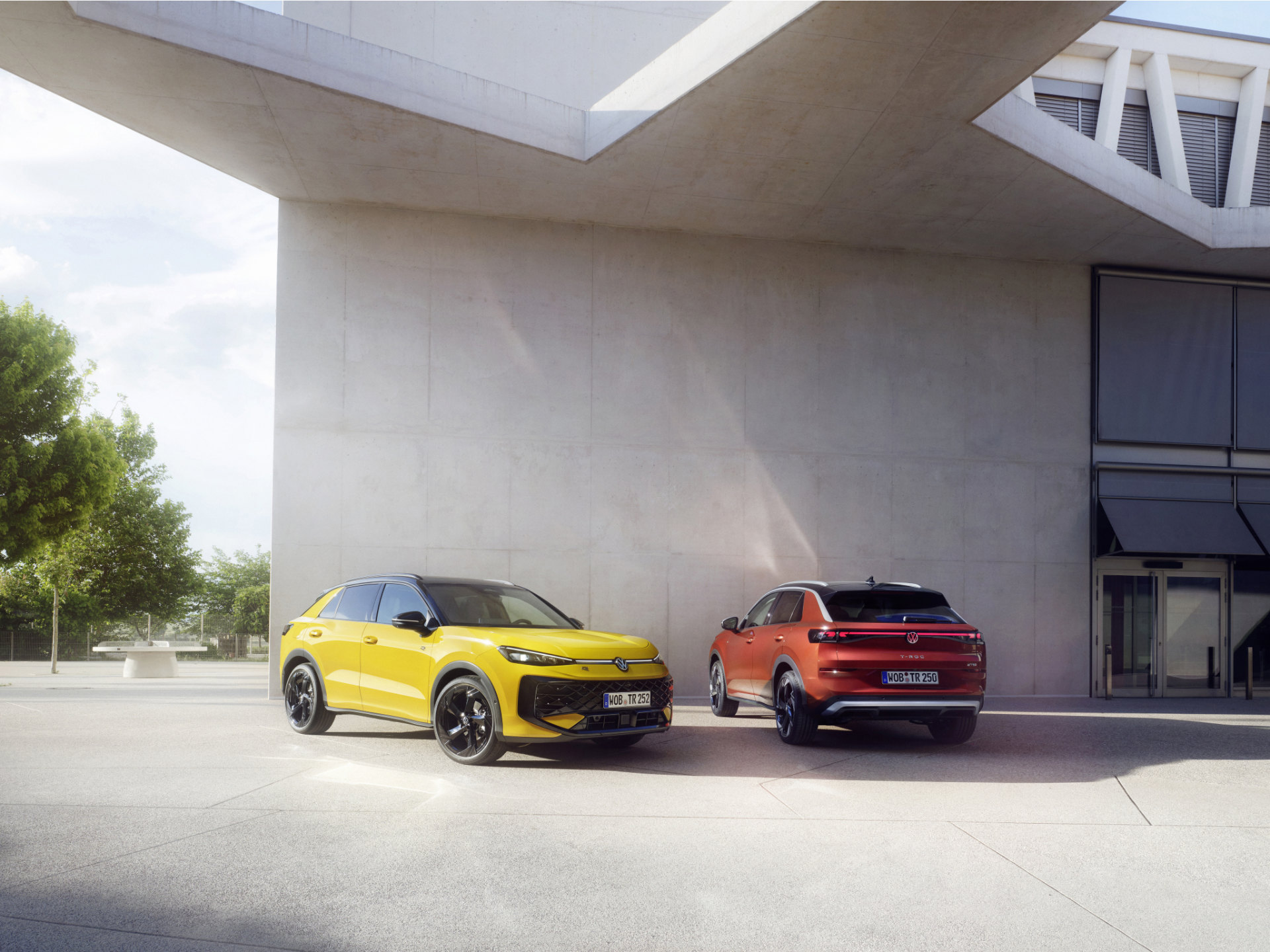 A yellow and a red Volkswagen T-Roc in front of some modernist architecture.